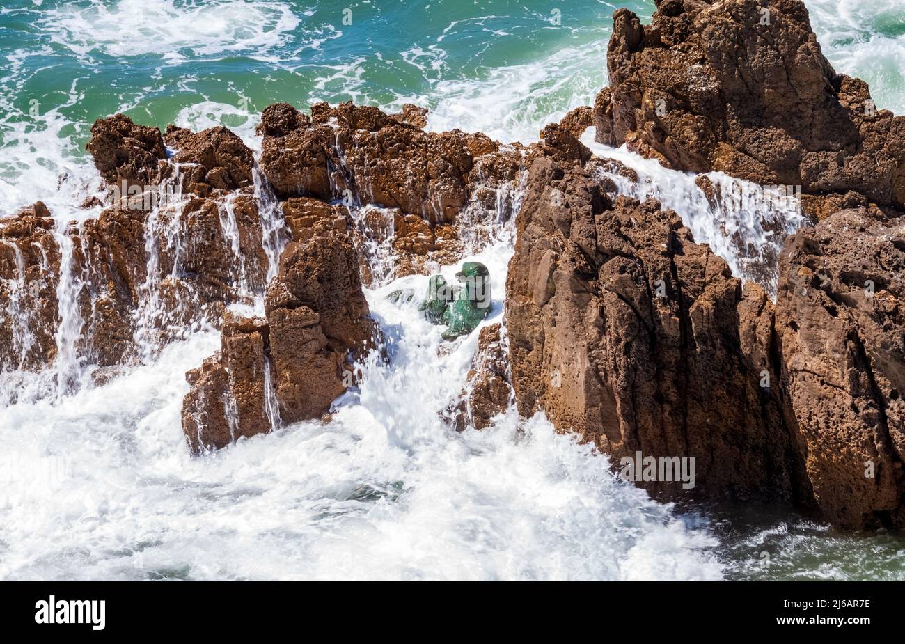 An einem sonnigen Tag stürzten Wellen auf Felsen mit Seelöwenskulpturen in Newport Beach, Kalifornien Stockfoto