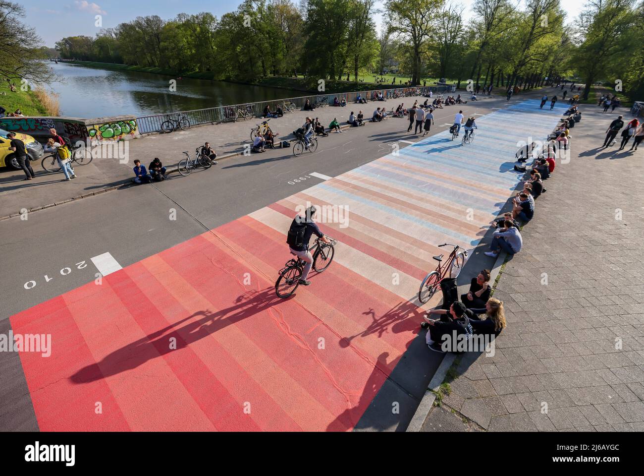 28. April 2022, Sachsen, Leipzig: Auf der Sächsischen Brücke sitzen Menschen neben sogenannten "Warming Stripes". Das Warnbild, basierend auf einem Modell des Wissenschaftlers Ed Hawkins, misst 70 x 6 Meter. Ein Farbspektrum aus blauen und roten Streifen zeigt, wie sehr sich die Erde in den letzten Jahrzehnten erwärmt hat. Umweltaktivisten wollen damit auf die rasanten Fortschritte der globalen Erwärmung aufmerksam machen. Foto: Jan Woitas/dpa Stockfoto