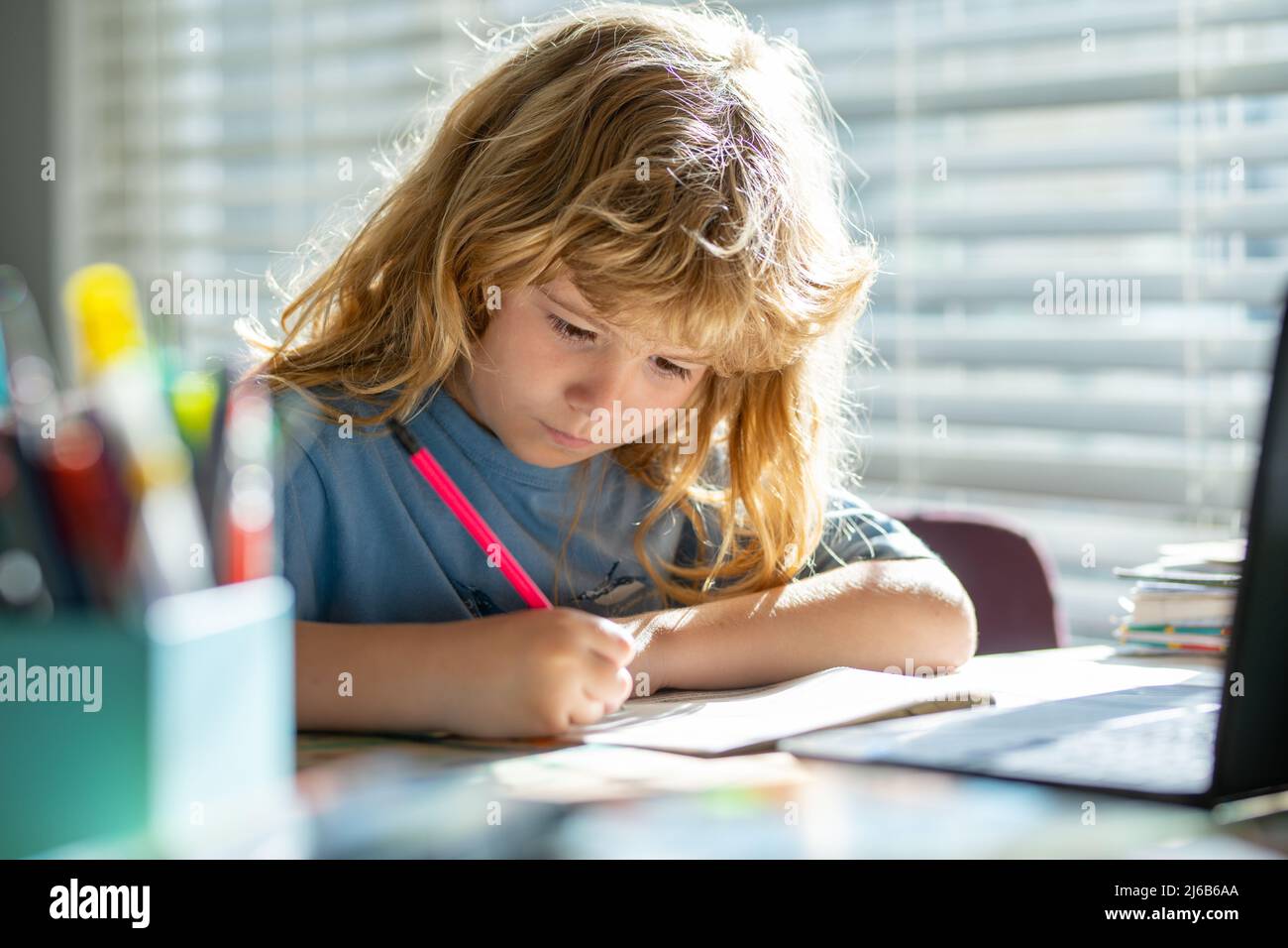 Kind schreibt in der Schule. Porträt eines Schuljungen, der auf dem Tisch sitzt und Hausaufgaben macht. Kind mit Bleistift und Schrift. Junge Zeichnung auf weißem Papier bei Stockfoto