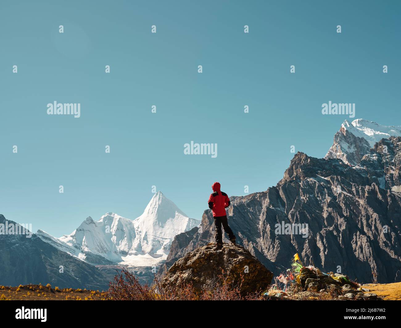 ein asiatischer Mann, der auf einem Felsen steht und den Berg Yangmaiyong (oder auf Tibetisch Jampayang) in der Ferne in Yading, Kreis Daocheng, Sichuan P, anschaut Stockfoto