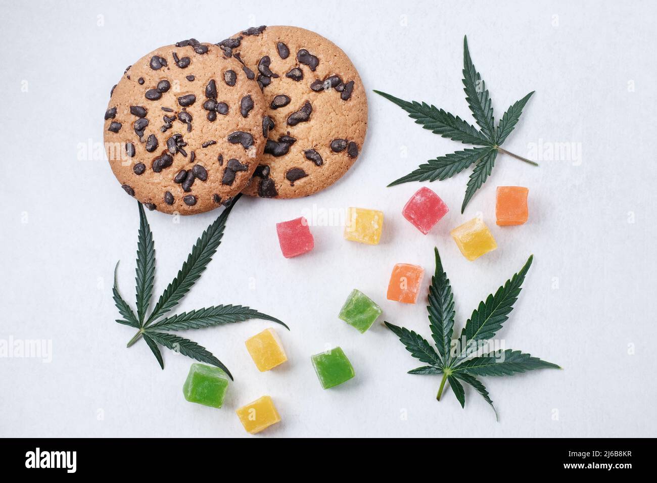 Amerikanische Cookies mit Cannabisextrakt. Süßigkeiten mit CBD-Öl. Marihuana Blätter auf weißem Hintergrund. Draufsicht, flach liegend. Stockfoto
