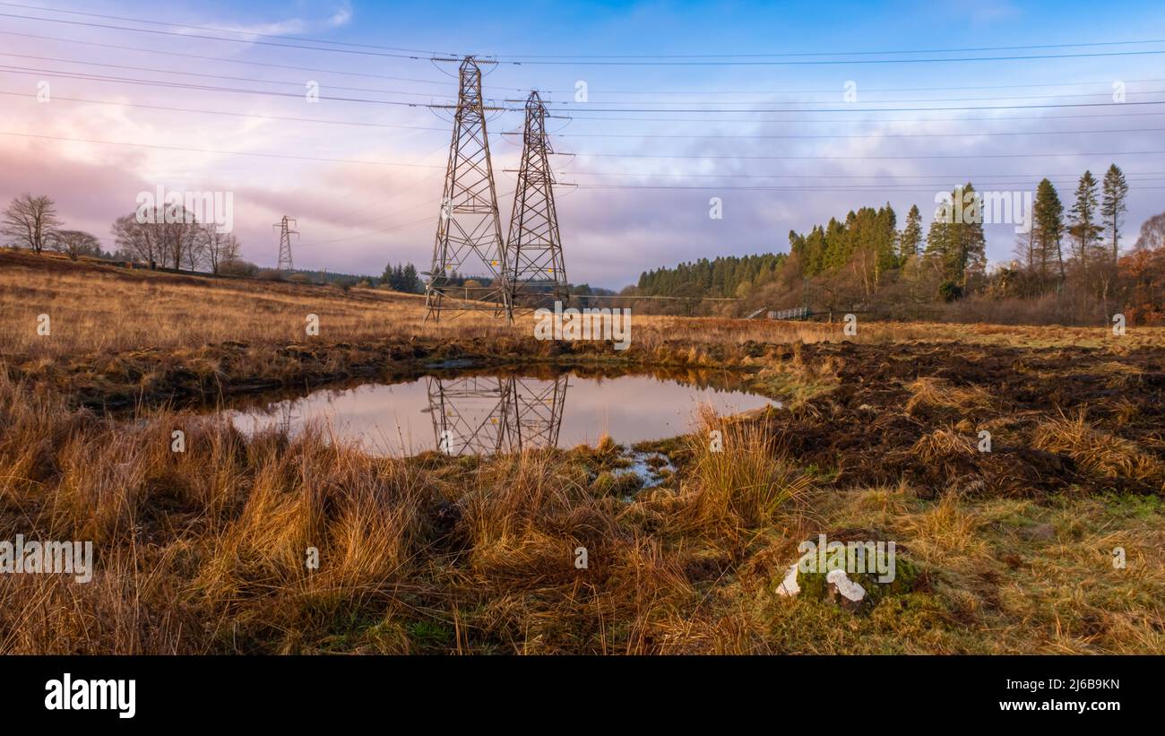 Strommasten mit Blick auf einen neuen künstlichen Farmteich oder schaben bei Sonnenuntergang im Winter nach Wildtieren, Carsphairn, Schottland Stockfoto