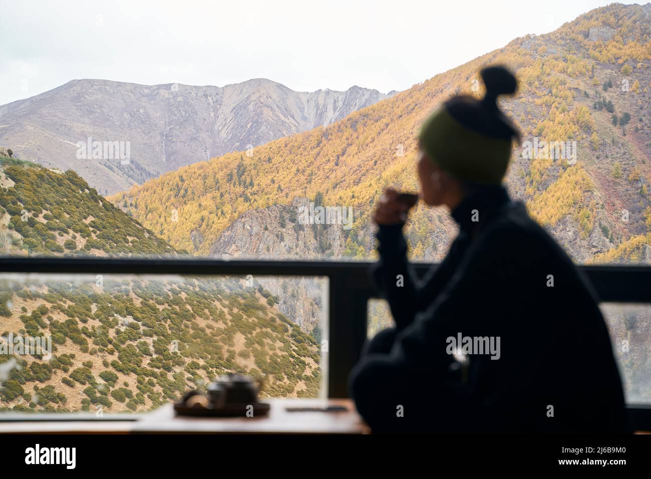 Silhouette einer asiatischen Frau, die auf dem Balkon sitzt und Tee trinkt und die Berge in der Ferne betrachtet Stockfoto