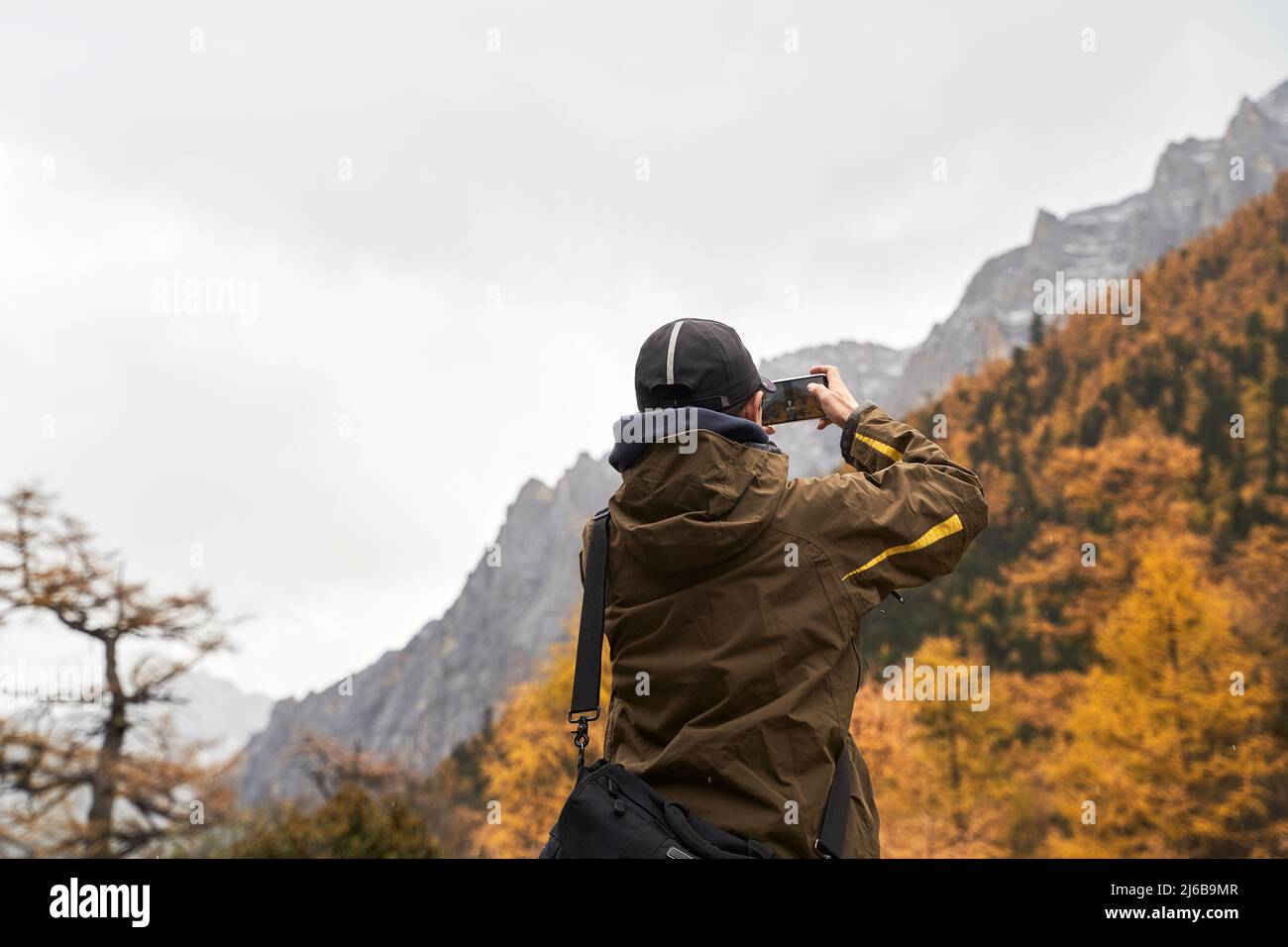 Rückansicht eines asiatischen männlichen Touristen, der mit dem Handy ein Landschaftsfoto von Berg- und Herbstlaub gemacht hat Stockfoto