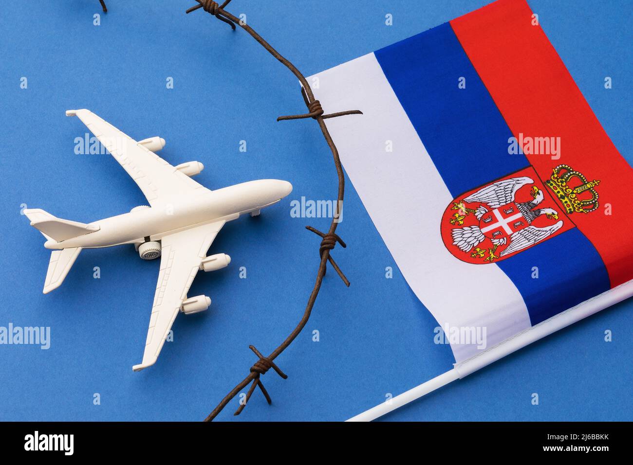 Spielzeugflugzeug, Flagge und Stacheldraht auf blauem Hintergrund, das Konzept der geschlossenen Luftgrenze Serbiens Stockfoto