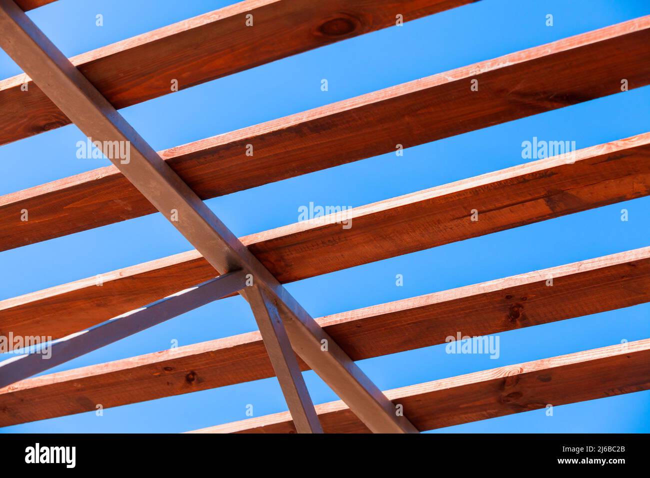 Hölzerne Dachbalken lagen auf einem Stahlrahmen, moderne Baukonstruktion steht an einem sonnigen Sommertag unter tiefblauem Himmel Stockfoto