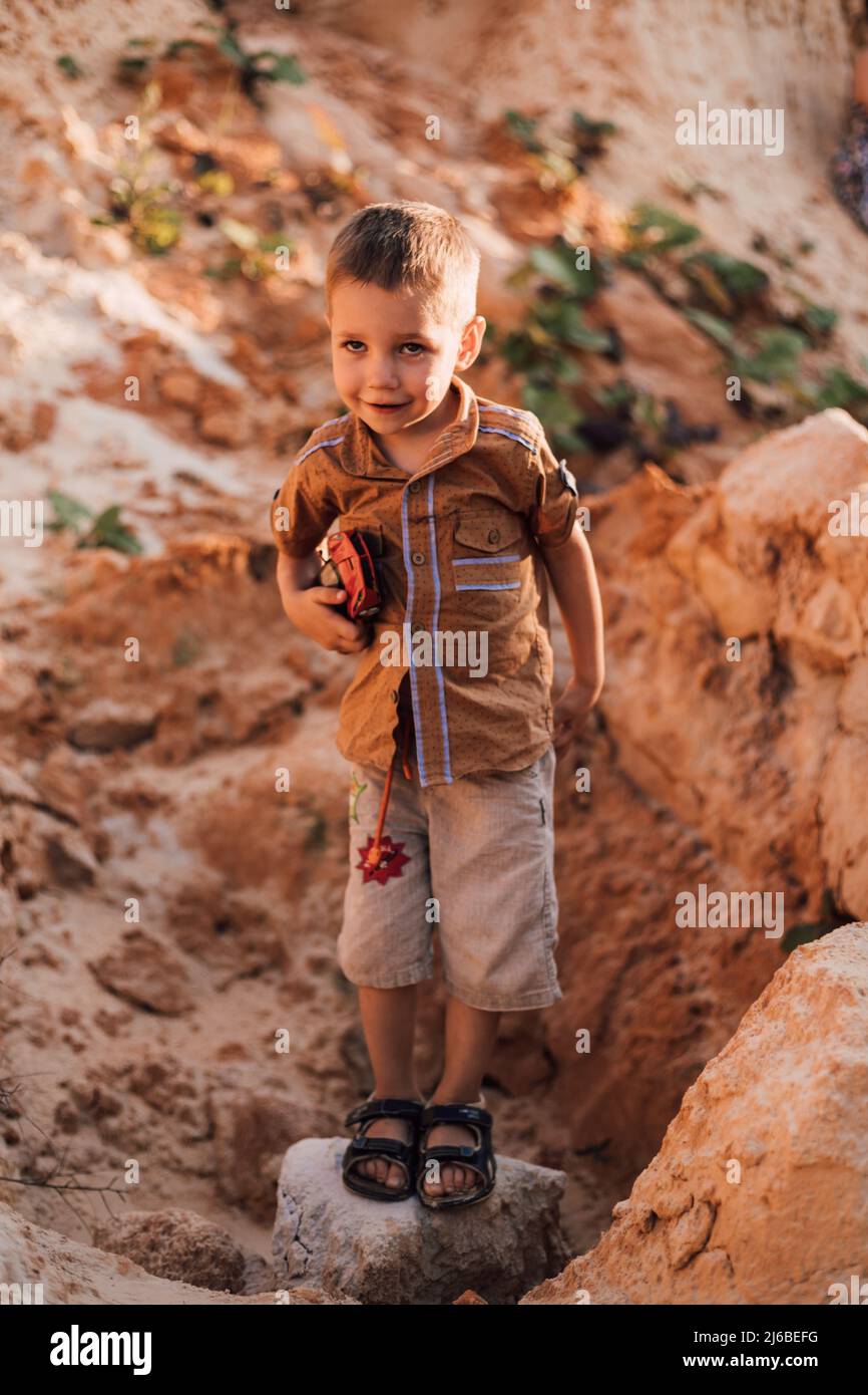 Ein kleiner Junge steht mitten im Sand und hält ein Spielzeug in den Händen Stockfoto