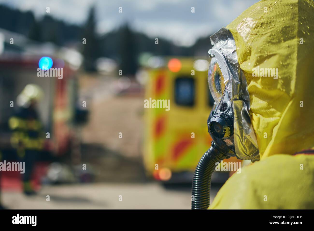 Mitglied des Biohazard-Teams des medizinischen Notdienstes in Schutzkleidung gegen Krankenwagen und Feuerwehrleute. Stockfoto