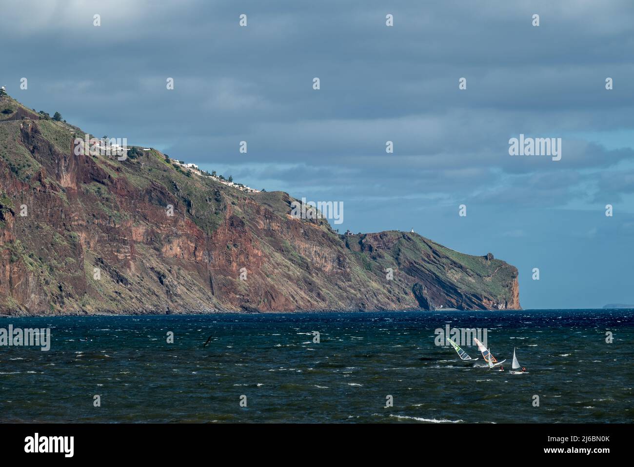 Windsurfer und Segler mit Madeiras südöstlicher Steilküste im Hintergrund. Stockfoto