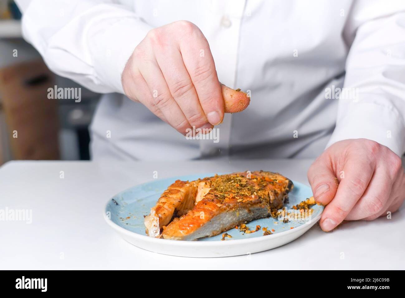 Der Koch streut das rote Fischsteak mit Gewürzen. Lachssteak liegt auf einem Teller Stockfoto