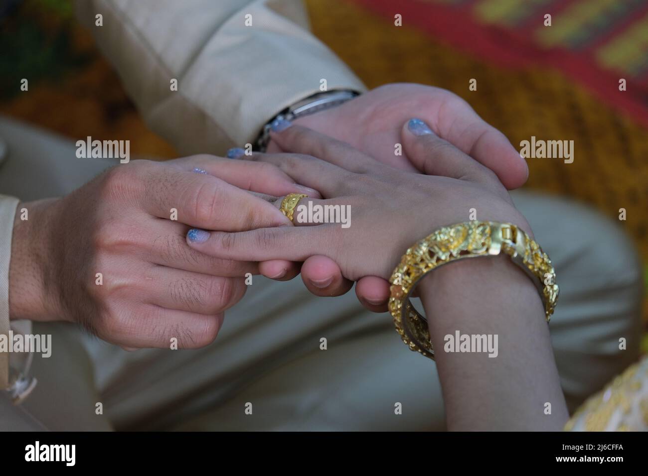 Thailändische Hochzeit: Ein Bräutigam legt einen goldenen Ring an den Finger einer Braut Stockfoto