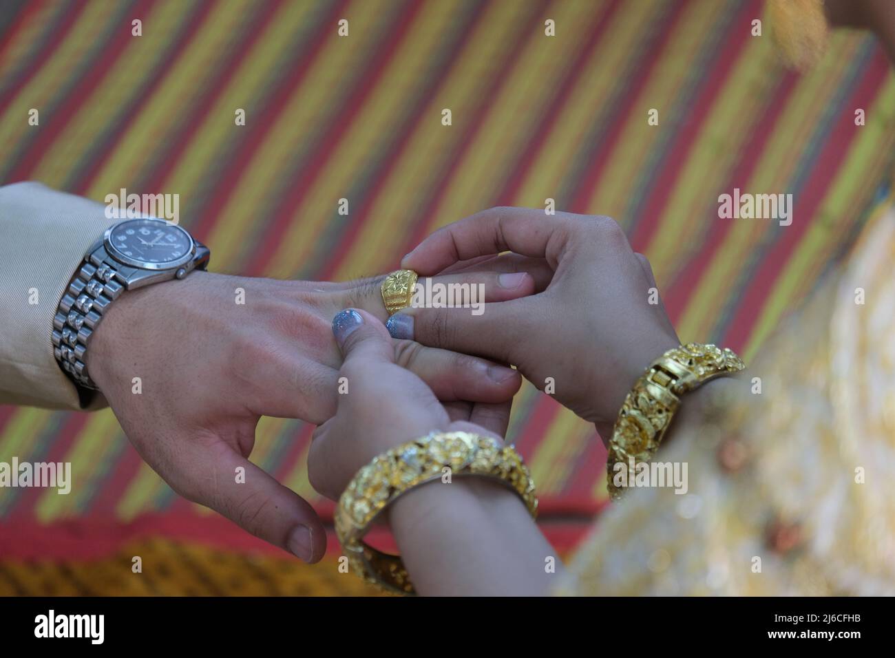 Thailändische Hochzeit: Die üppig geschmückte Braut legt einen goldenen Ring an den Finger des Bräutigams Stockfoto