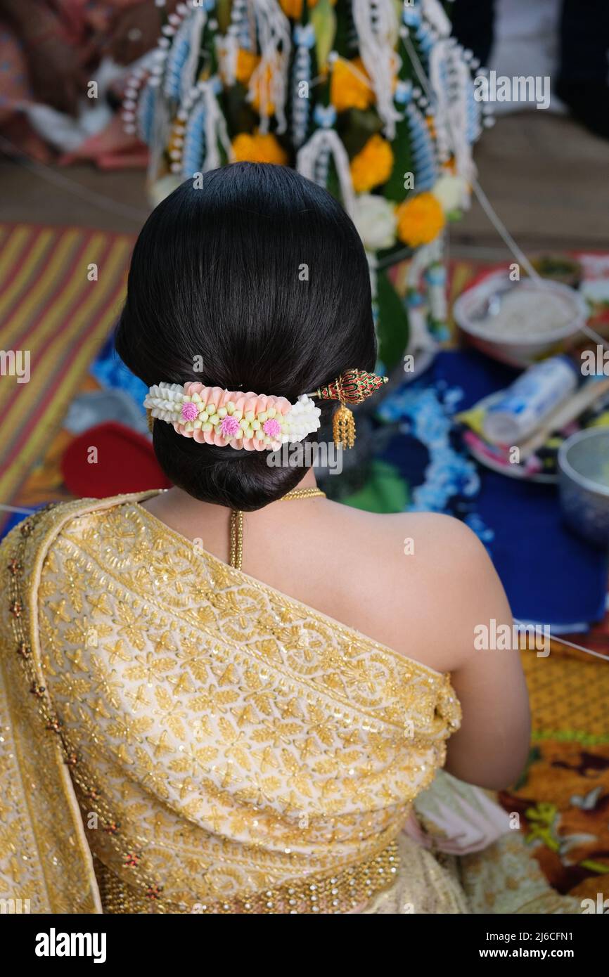 Thailändische Hochzeit: Eine sitzende Braut, üppig verziert mit Gold und Blumen Stockfoto