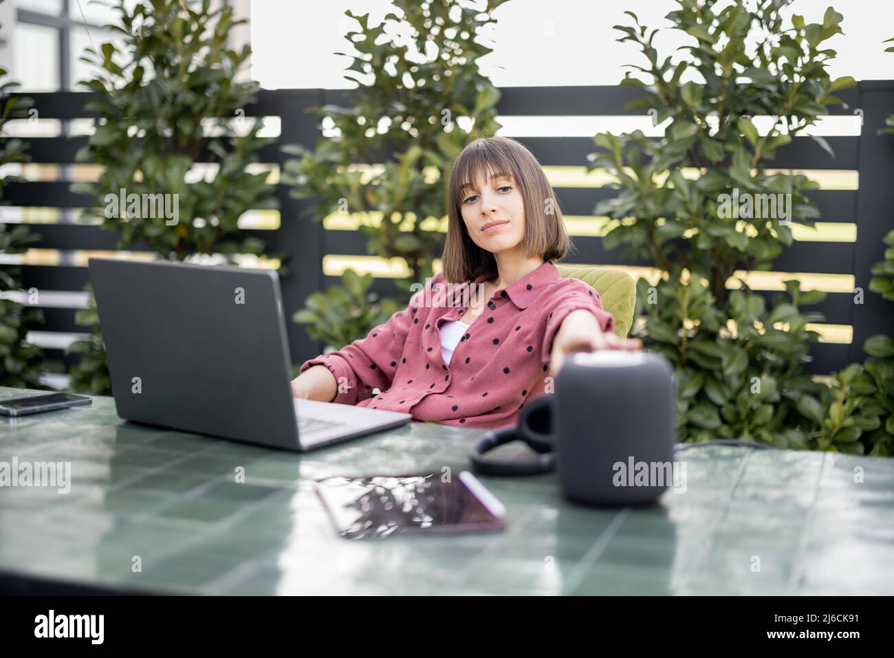 Frau berührt den smarten Lautsprecher, während sie am Tisch sitzt und im Garten arbeitet Stockfoto