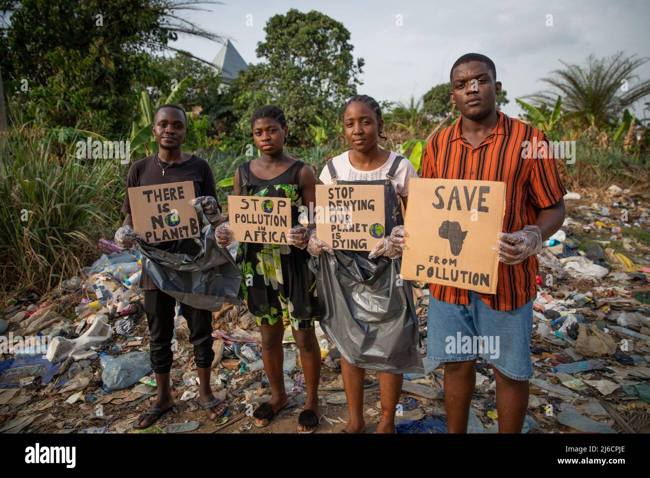 Eine Gruppe junger afrikanischer Aktivisten protestiert mit Zeichen gegen Umweltverschmutzung, sie befinden sich vor einer illegalen Deponie und sind dabei, den was zu entfernen Stockfoto