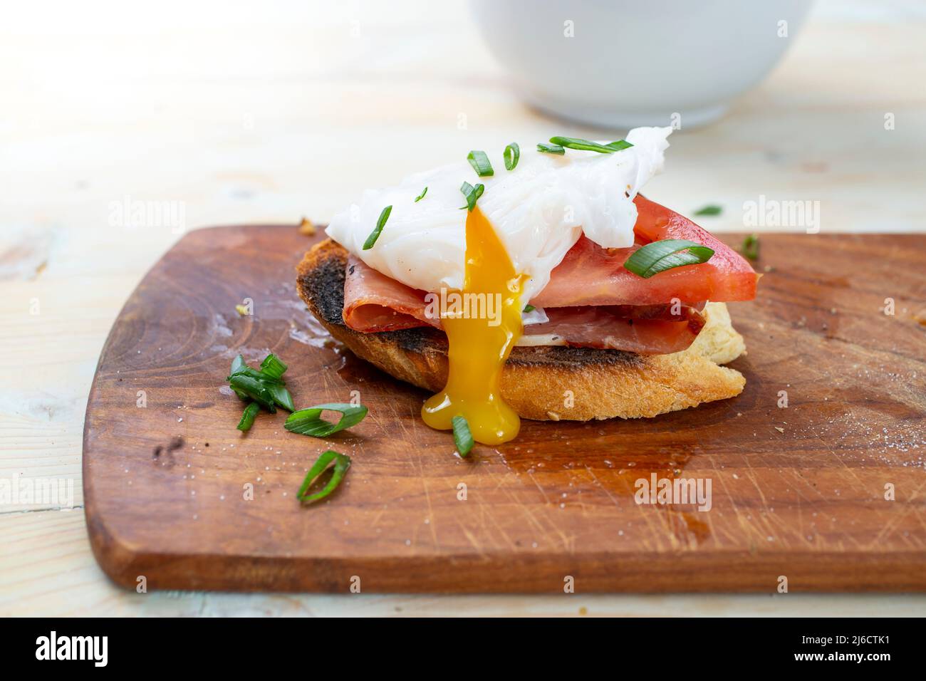 Pochiertes Ei mit tropfendem Eigelb, Schinken- und Tomatenscheibe, auf Toastbrot, Seitenansicht aus nächster Nähe Stockfoto