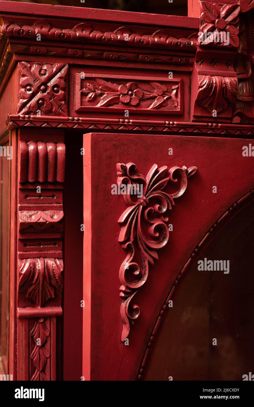 Nahaufnahme eines gemusterten, alten, renovierten Schranks mit schönen, handgeschnitzten Ornamenten und Holzhauswänden im Hintergrund. Werkstatt für Möbelrestaurierung Stockfoto
