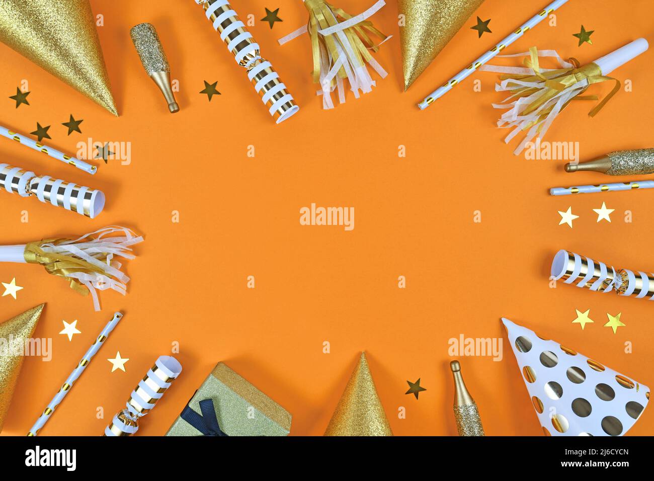 Partyobjekte wie Papierhüte, Konfetti, goldene Champagnerflaschen und Sternkonfetti bilden den Rahmen um den orangefarbenen Hintergrund Stockfoto