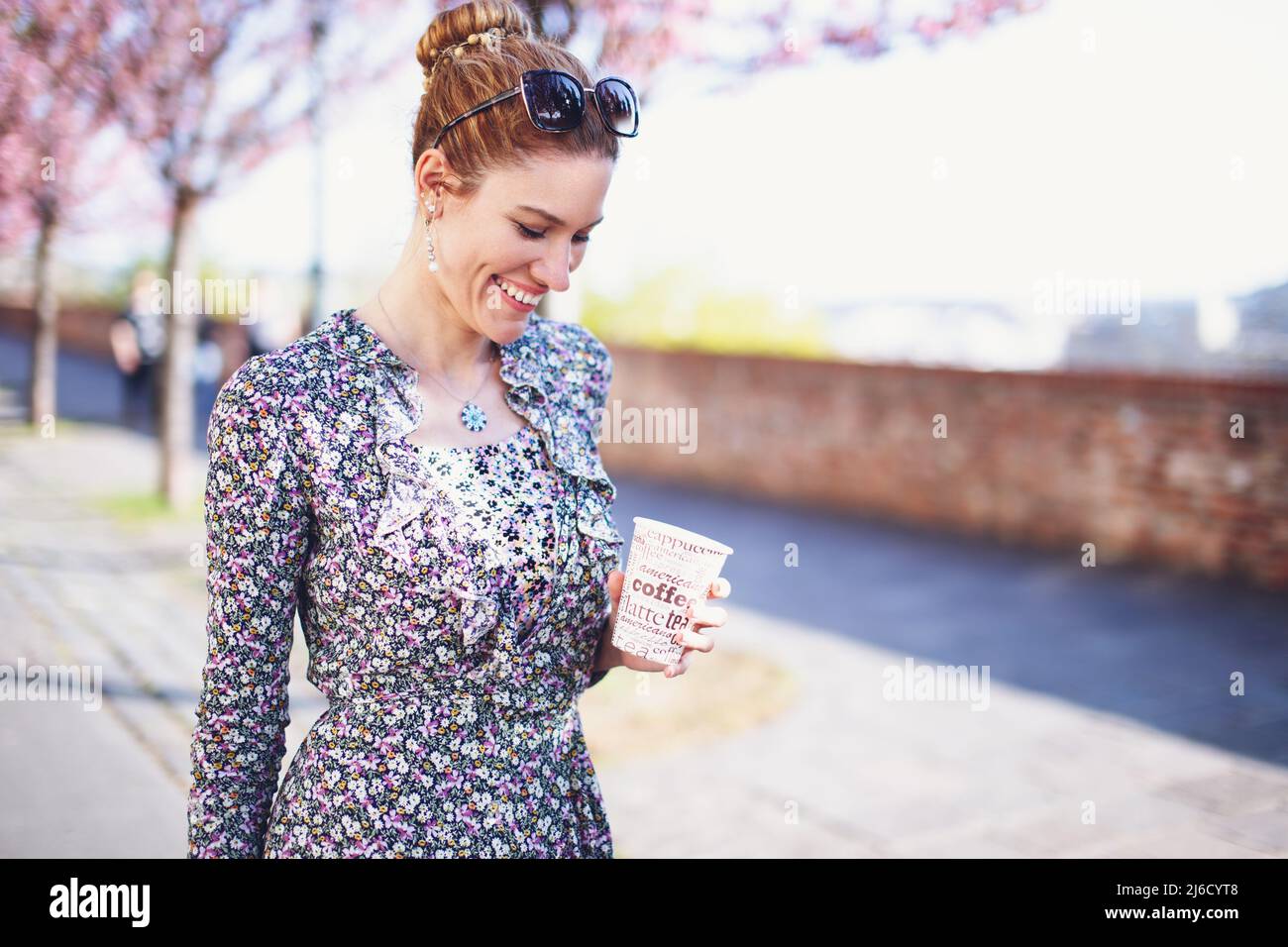 Glückliche junge Frau lächelt mit einer Tasse Kaffee im Freien Stockfoto