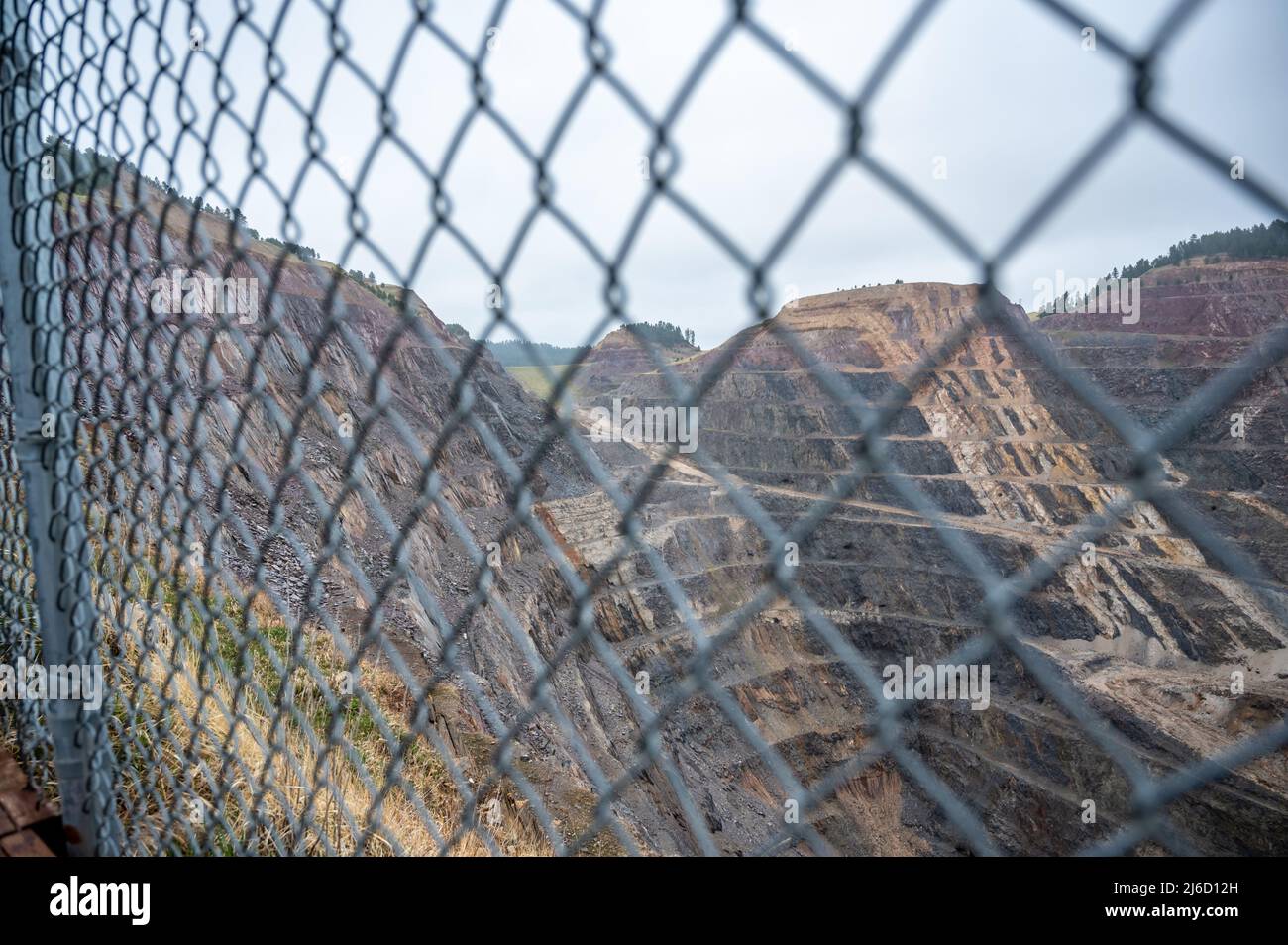 Tagebau im Hintergrund mit einem verschwommenen Kettengliederzaun im Vordergrund. Stockfoto