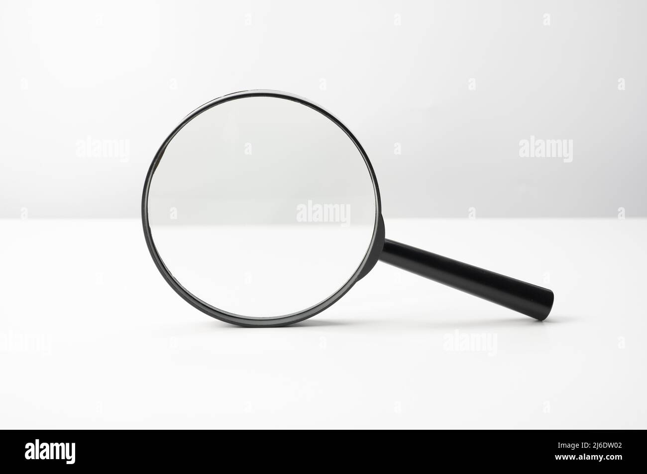 Lupe schwarz auf weißem Tisch. Recherchieren, suchen oder untersuchen. Frontansicht. Schwarzes Vergrößerungsglas mit weichem Schatten auf wh Stockfoto
