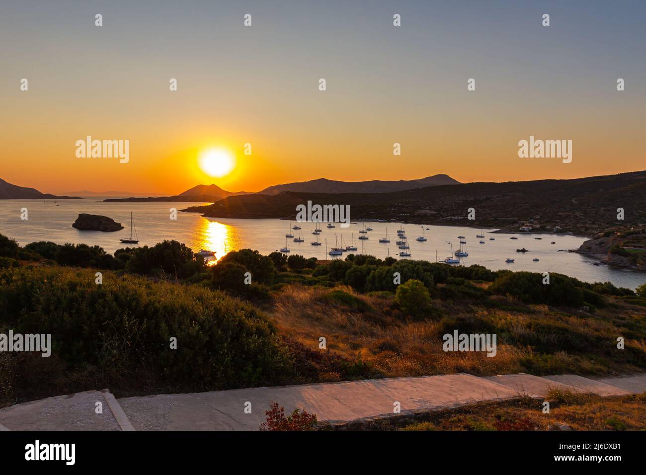 Sonnenuntergang in Lavrio Bay. Die rot-gelb leuchtende Sonne sinkt am Horizont. Boote ankern und liegen vor der Küste. Romantische Szene im Cyladen-Archipel Stockfoto