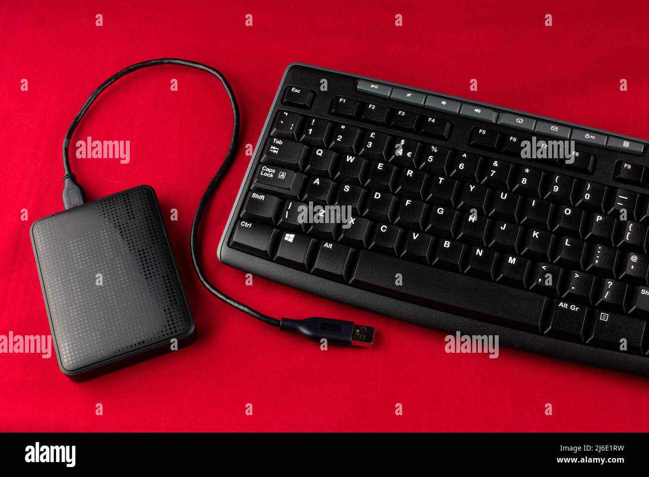 Computertastatur und externe Festplatte mit Kabel auf rotem Hintergrund Stockfoto
