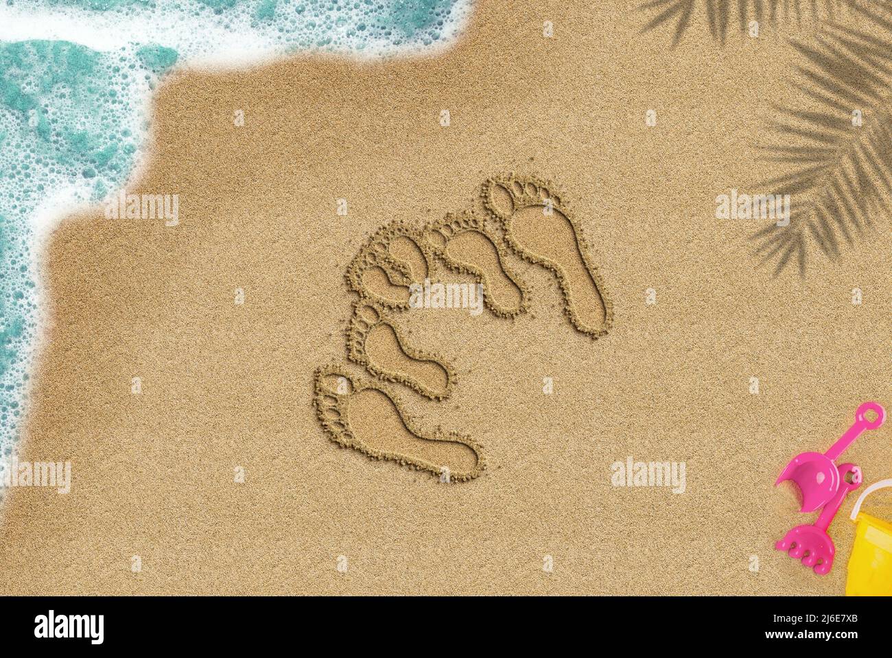 Familienfußabdruck am Sandstrand, Reise- und Familienreisekonzept, Blick von oben auf den Sandstrand, Idee der Sommerzeit, Palmschatten und Meereswellen-Spielzeug-Komposition Stockfoto