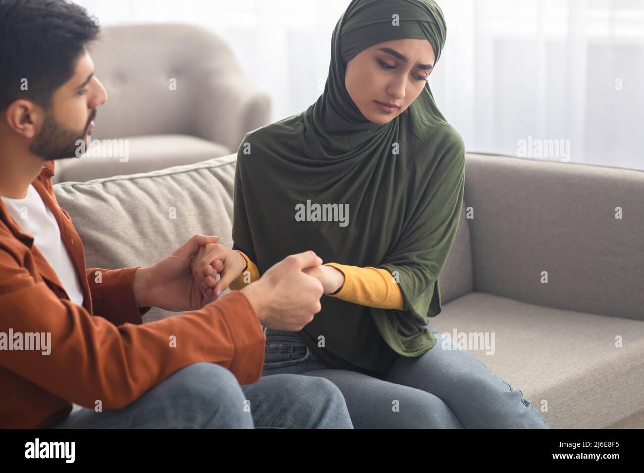 Unglückliches Paar Aus Dem Nahen Osten, Das Hände Auf Dem Sofa Im Wohnzimmer Hält Stockfoto