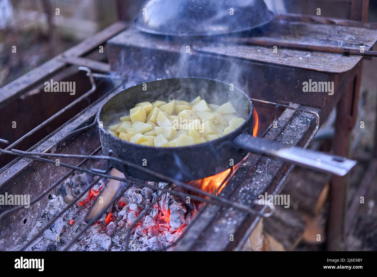 Gebratene Kartoffeln auf offenem Feuer. Die alte Bratpfanne steht auf dem Regal unter dem Feuer Stockfoto