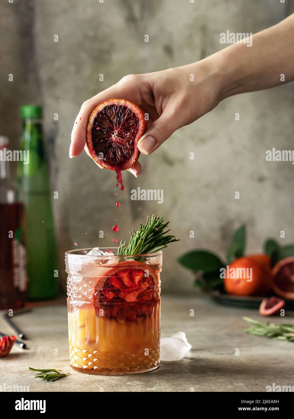 Weibliche Hand drückt Saft aus Orange in ein Glas mit köstlichen Eiscocktail . Gefrorene Tropfen Stockfoto