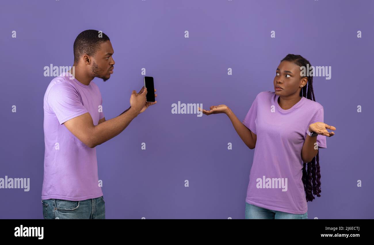Wütender schwarzer Mann, der seine Freundin auf dem Handy überprüft Stockfoto