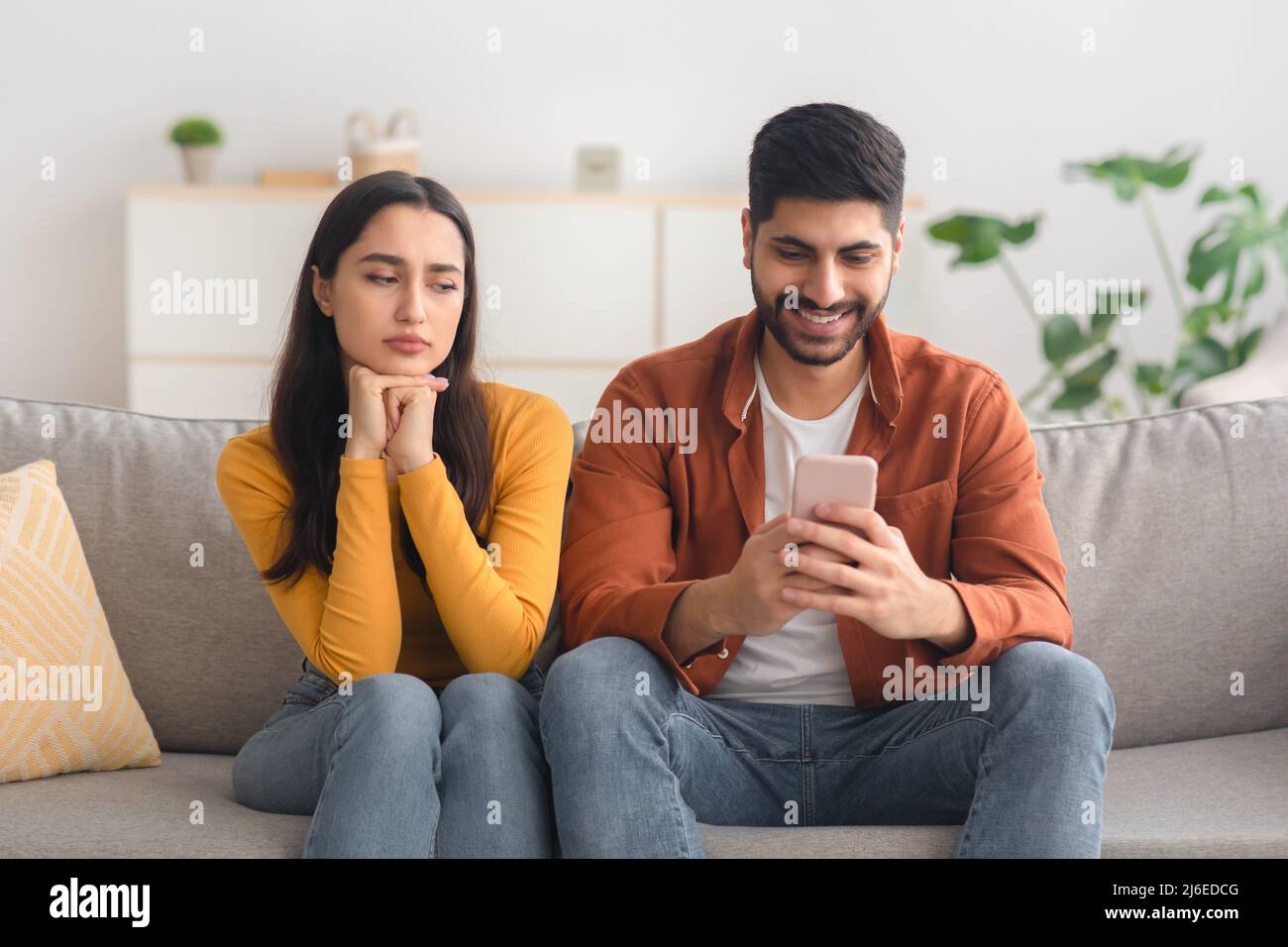 Arabisch Frau Ahnend Untreue Blick Auf Ehemann, Während Texting Indoor Stockfoto