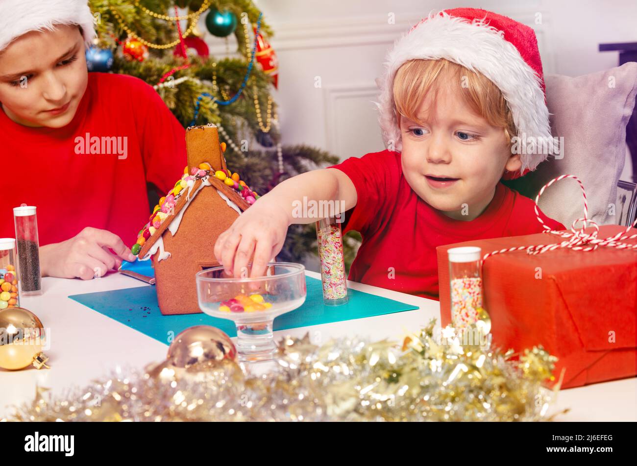Kleiner Kleinkind Junge nimmt Süßigkeiten auf das Lebkuchenhaus zu setzen Stockfoto