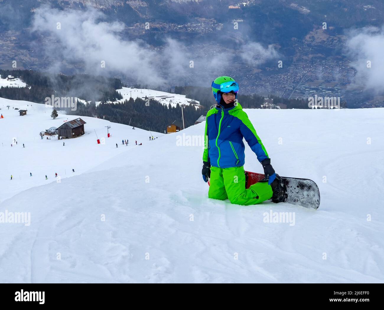 Snowboarderkind steht auf den Knien im Schnee in den Bergen Stockfoto