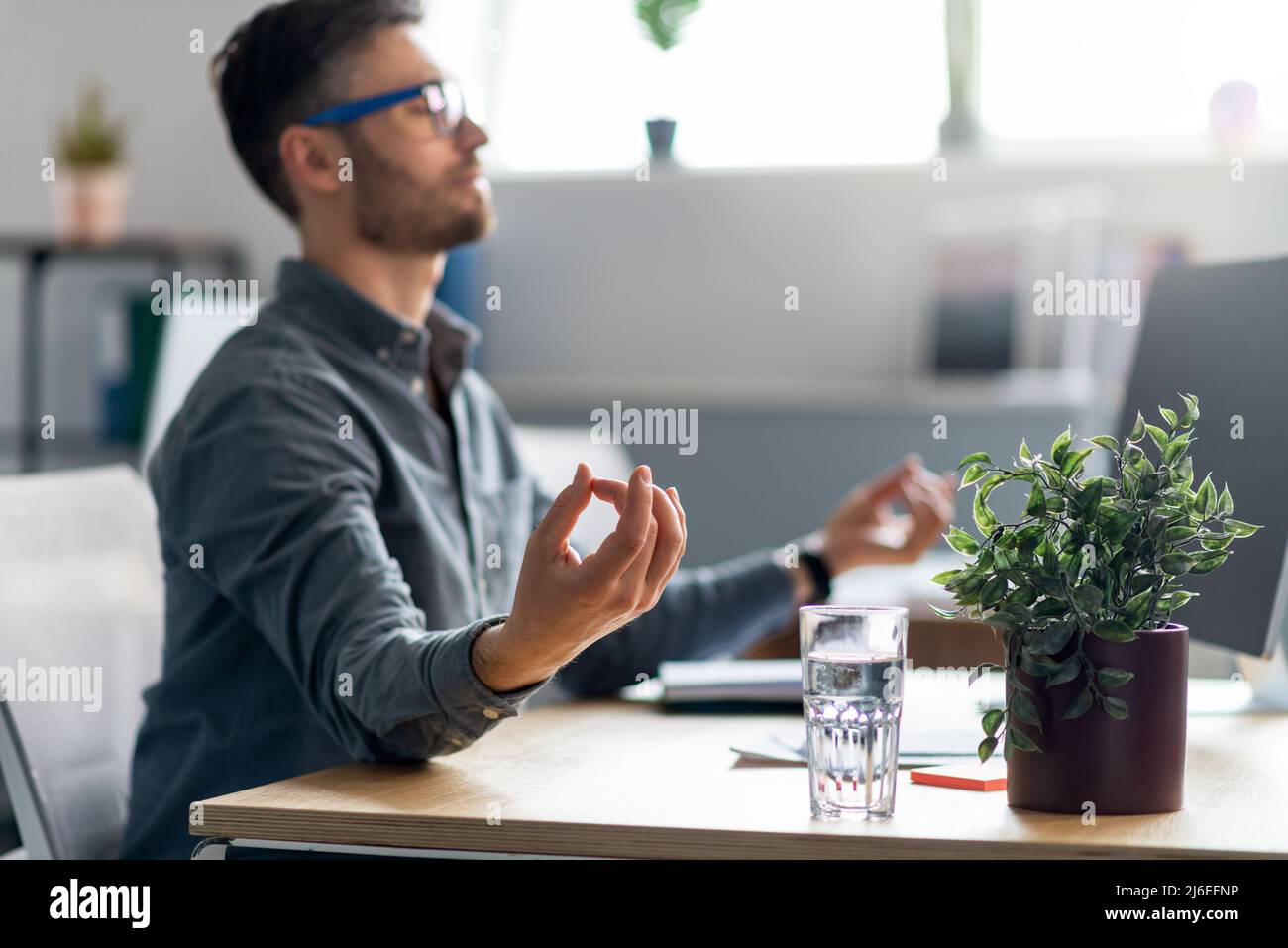Ruhiger, reifer Büroangestellter, der mit einem Laptop am Schreibtisch sitzt, meditiert und sich während des stressigen Arbeitstages entspannt Stockfoto
