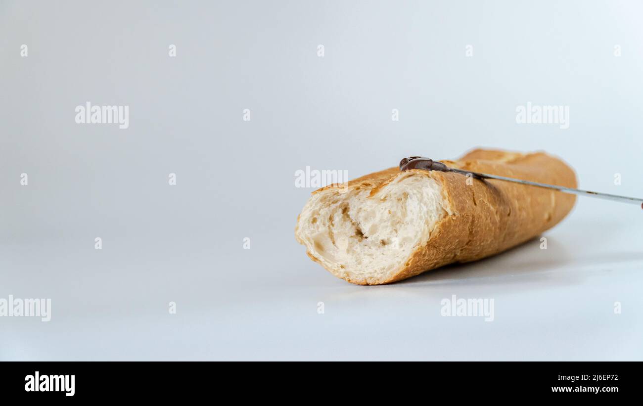 Stück Baguette Brot isoliert auf weißem Hintergrund mit Messer auf Schokoladencreme mit Haselnuss. Stockfoto