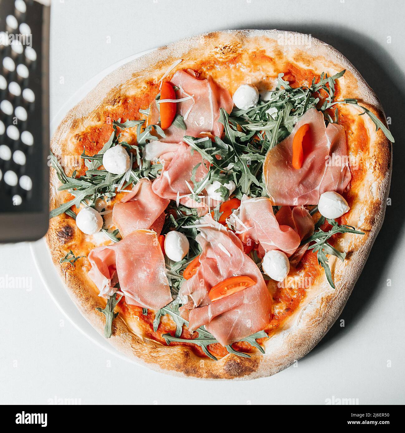 Traditionelle italienische Pizza mit Schinken, Käse, Mozzarella und Reibe auf einem weißen Tisch, Restaurantküche Konzept Stockfoto