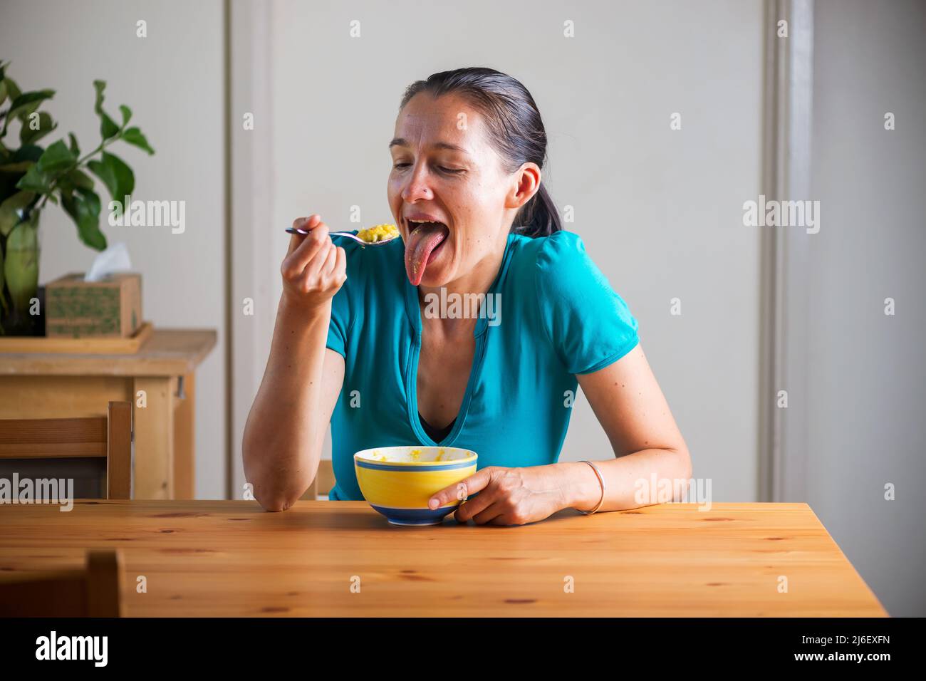 Frau, die Kitchari zum Frühstück isst und lustige Gesichter macht. Stockfoto