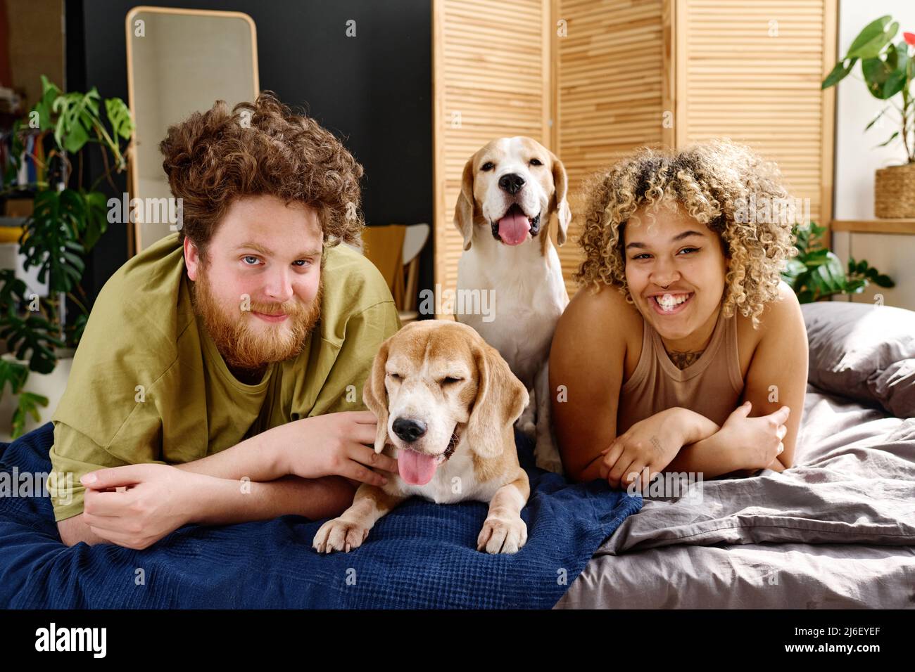 Porträt eines multiethnischen jungen Paares, das mit seinem Haustier auf dem Bett im Schlafzimmer liegt und die Kamera lächelt Stockfoto