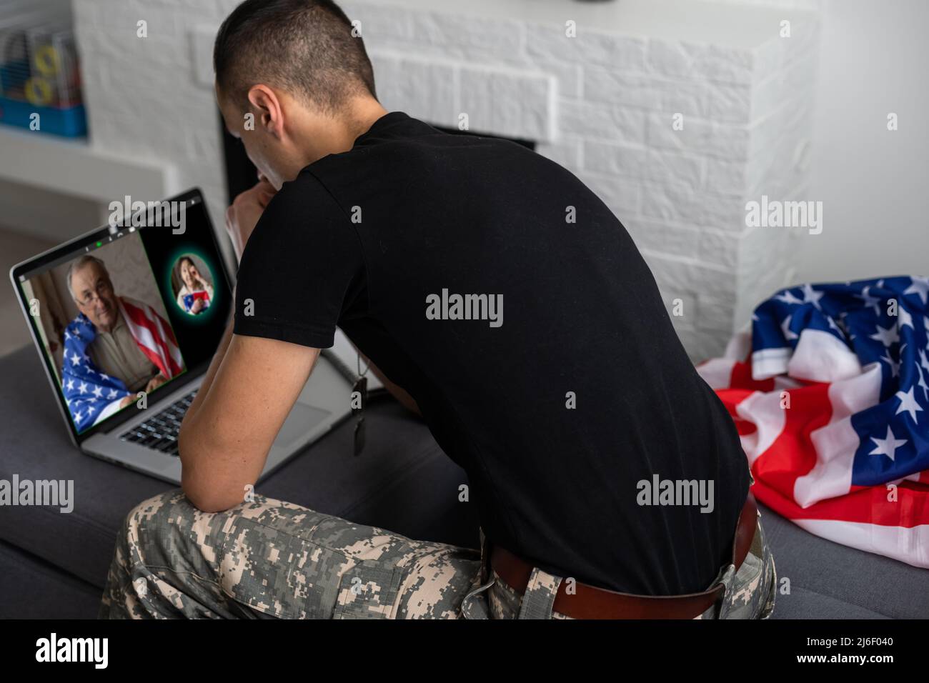 Patriotischer Militärangehöriger im Headset, der in der Nähe der amerikanischen Flagge auf einen Laptop schaut Stockfoto