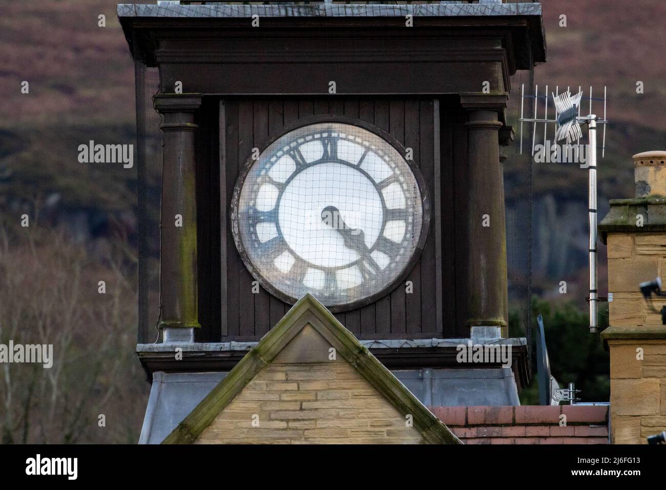 Weißes Zifferblatt auf einem Uhrturm mit römischen Ziffern und dem Minutenzeiger, der den Stundenzeiger überlappt, West Yorkshire, England, Großbritannien Stockfoto