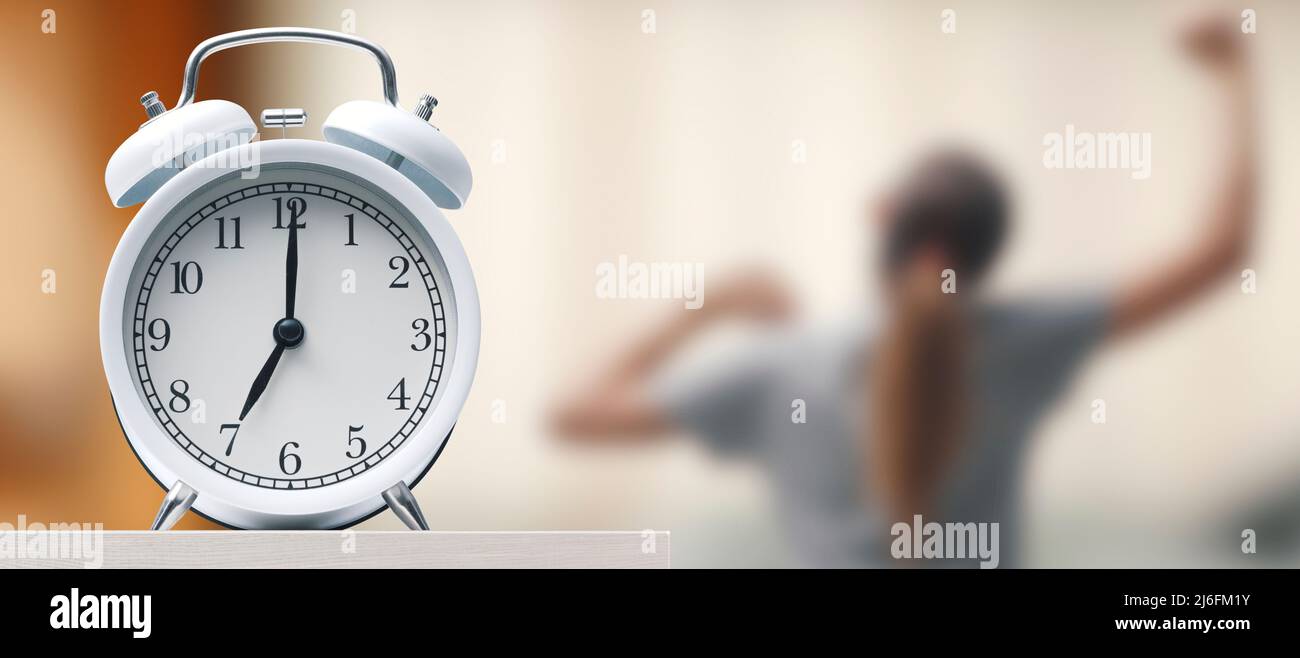 Wecker auf dem Nachttisch, eine Frau steht auf und streckt sich Stockfoto