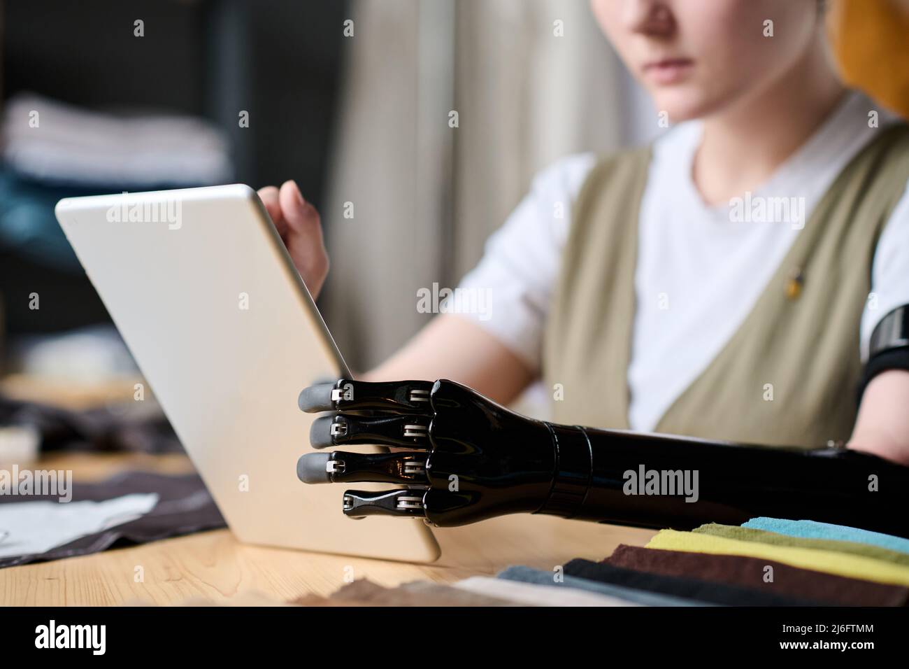 Schwarze myoelektrische Armprostthese von Näherinnen, die ein Tablet benutzen, während sie am Arbeitsplatz sitzen und im Internet nach authentischen Ideen suchen Stockfoto