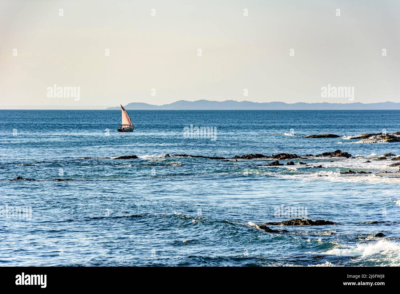 Rudimentäres Fischerboot, das während des Sonnenuntergangs durch die ruhigen Gewässer der Todos os Santos Bay in der Stadt Slavador in Bahia fährt Stockfoto