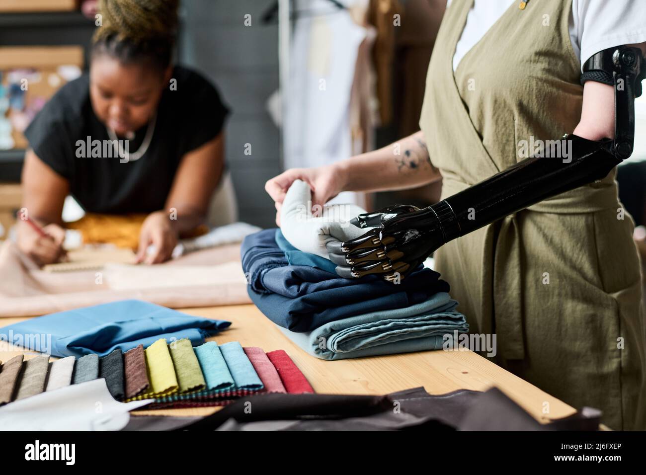 Junge Frau mit myoelektrischen Armprothesen Falten und Stapeln Textil für neue Saison Sammlung von Kleidung gegen Kollegen Stockfoto