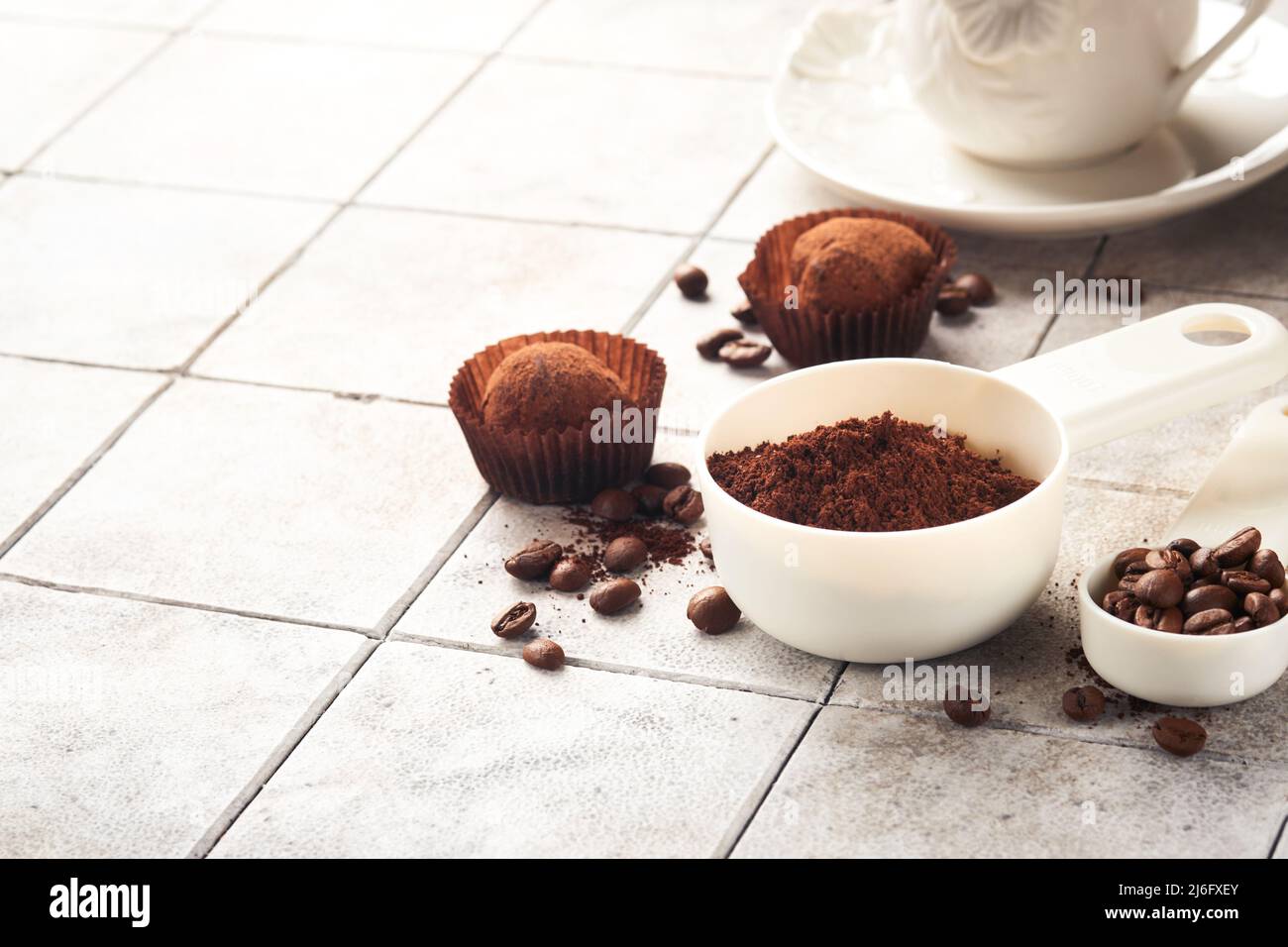 Hintergrund für Kaffee. Messlöffel mit gemahlenem Kaffee, Bohnen, Tasse und süßen Schokoladentrüffeln auf alten Kacheln geknackt Tischhintergrund. Hintergrund der Speisen. Stockfoto