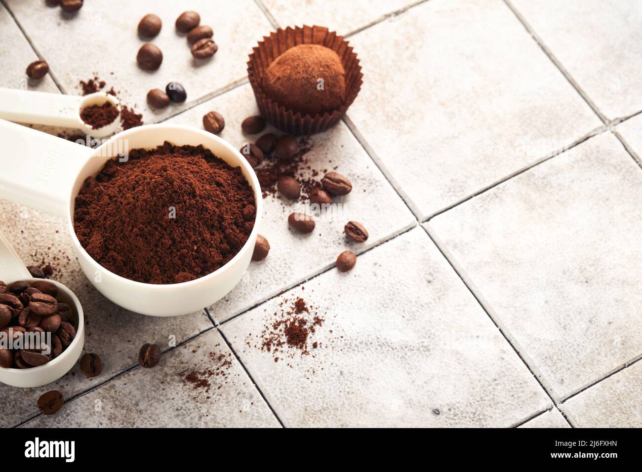 Hintergrund für Kaffee. Messlöffel mit gemahlenem Kaffee, Bohnen, Tasse und süßen Schokoladentrüffeln auf alten Kacheln geknackt Tischhintergrund. Hintergrund der Speisen. Stockfoto
