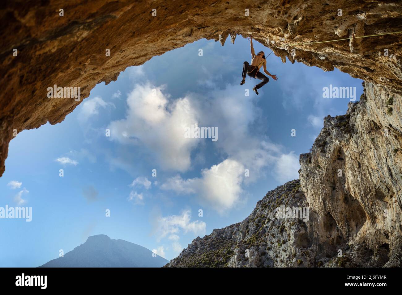 Männlicher Bergsteiger, der mit einer Hand an einer Klippe gegen den Himmel hängt Stockfoto