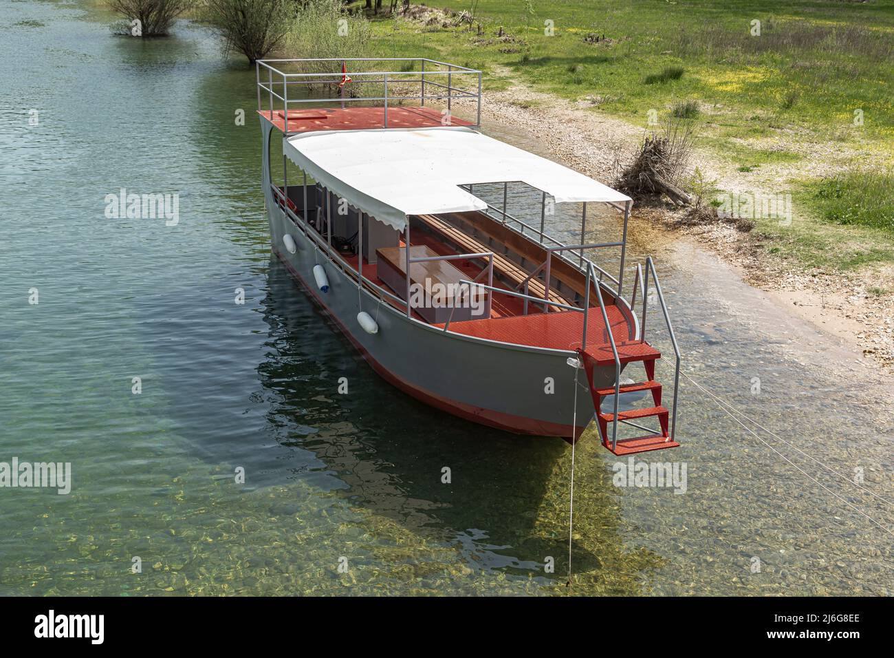 Rot und grau Vergnügen Handwerk Segelboot an der Seite eines klaren grünen Flusses vertäut Stockfoto